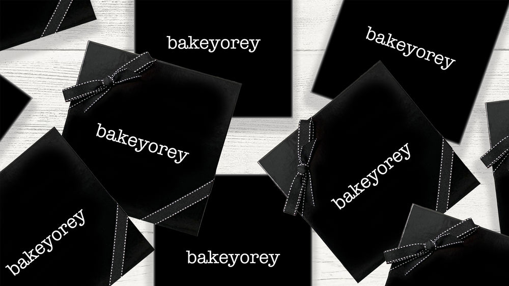 A group of black gift boxes with black ribbon with white logo reading Bakeyorey on a gray wood tabletop