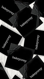 A group of black gift boxes with black ribbon with white logo reading Bakeyorey on a gray wood tabletop